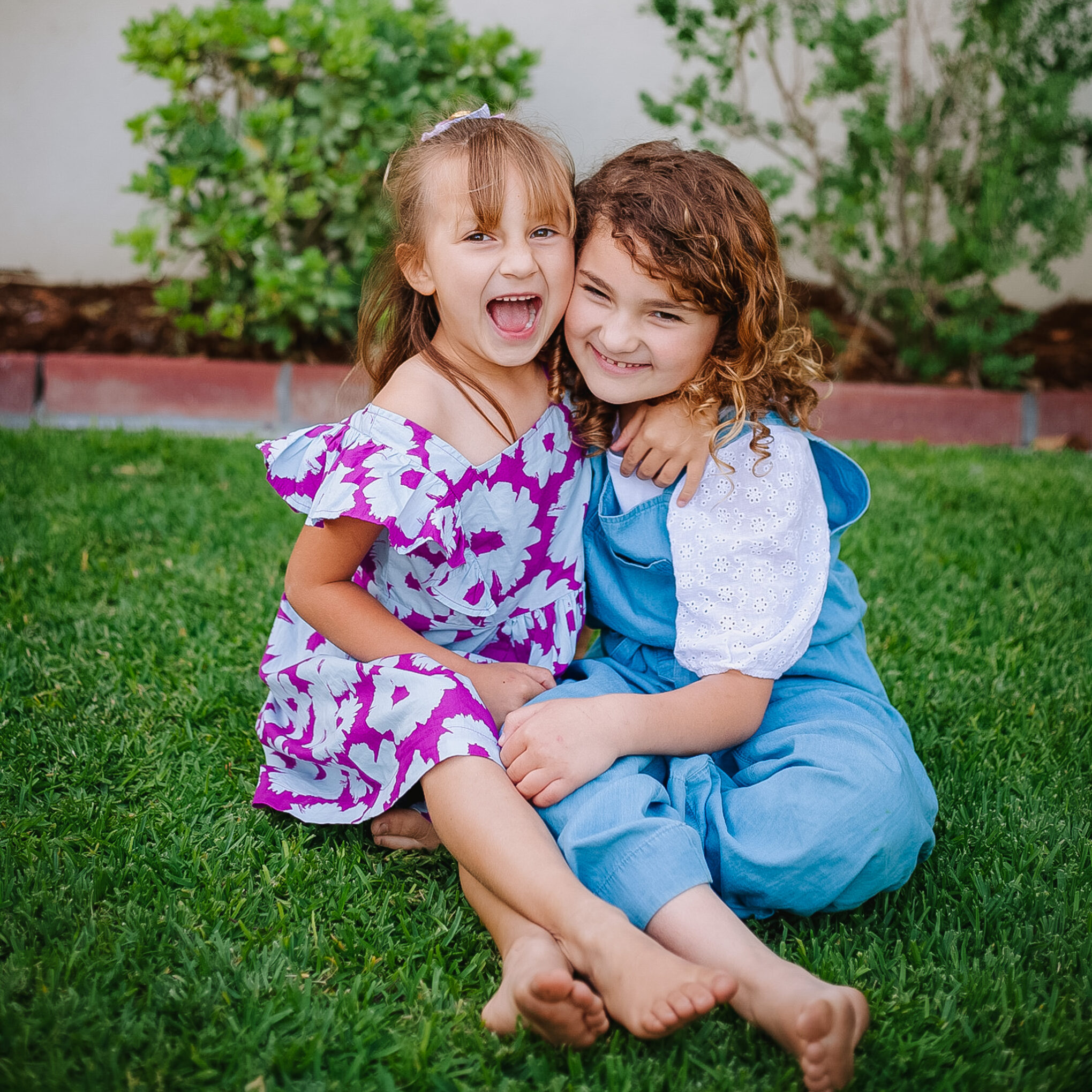 Sisters sitting on lawn for photoshoot enjoying each other during golden hour.
